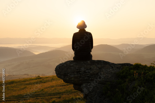 Alone tourist on the edge of the mountain hill against the backdrop of an incredible sunset mountains landscape
