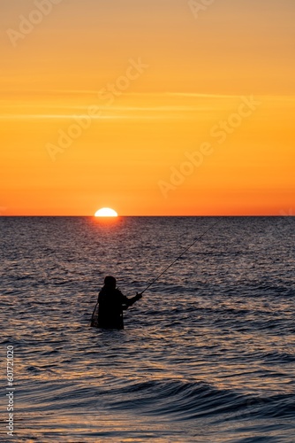 Silhouette eines Angler in wasserdichten Hosen welcher  vor einem traumhaften orangen Sonnenuntergang in der Ostsee angelt / fischt . Er steht mitten im Wasser der Ostsee.