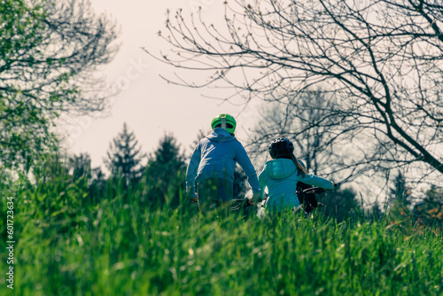 Group of kids riding bikes in nature on a lush green hillside on a sunny spring day, bike helmets on cyclists' heads, sunny spring weather, kids traveling, authentic healthy lifestyle