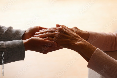 Cropped studio shot of elderly woman and female geriatric social worker holding hands. Women of different age comforting each other. Close up, background, copy space. photo