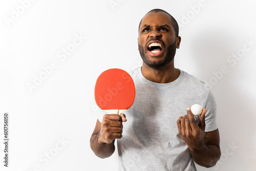 Dark-skinned adult man poses with a ping-pong racket and a ball. The man has an expression of anger, disappointment, discouraged with the championship. Concept of ping-pong in Africans. photo