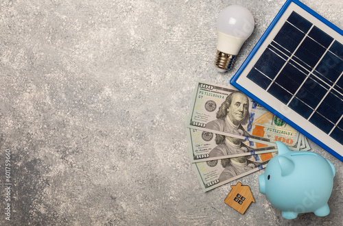 Flat lay composition with solar panel, led lamp. house model and piggy bank on a marble background. The concept of saving money and clean energy. The concept of ecology and sustainable development. photo