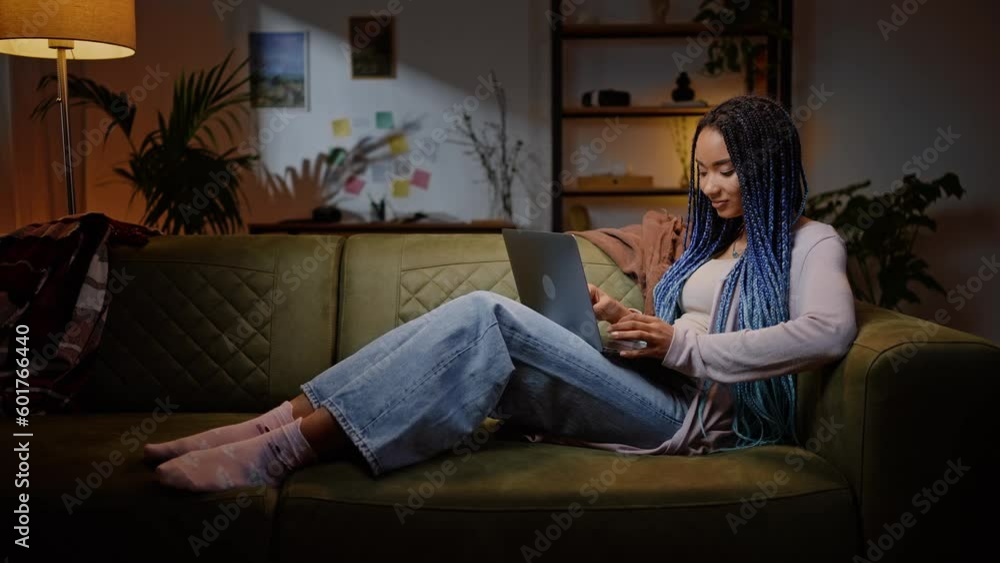 Confident successful young African woman typing text on laptop, sitting relaxed on the sofa at home Confident successful young African woman typing text on laptop, sitting relaxed on the sofa at home