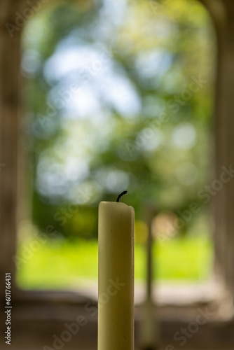 An unlit candle in a church, with defocused countryside through the window behind