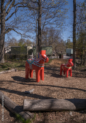 Traditional kurbits painted orange wood horses at a playground in a park, a sunny early summer day in Stockholm