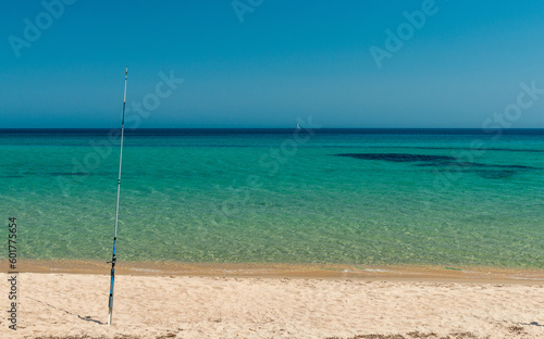 Fishing rod on a beach of golden sand, blue sky and turquoise sea. Leisure destination on the Mediterranean in Sardinia, Italy