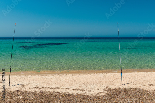 Fishing rods on a beach of golden sand, blue sky and turquoise sea. Leisure destination on the Mediterranean in Sardinia, Italy.