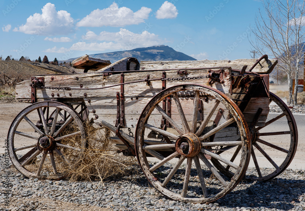 Worn weathered buckboard wood wagon with mountains and blue sky background. Wood wheels are prominent.