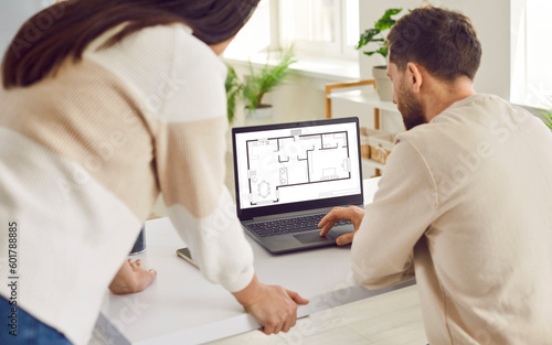 Two architects or interior designers working with design project of apartment on laptop. Couple looking at blueprint of architecture plan apartment set discussing engineering floor plan.