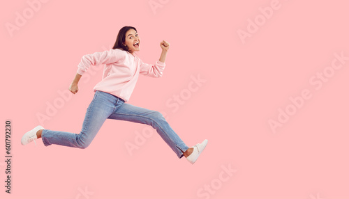 Seasonal discounts. Funny energetic young woman rushes to shopping center in hurry for crazy discounts on sales. Woman in casual clothes running isolated on pink background. Web banner. Copy space.