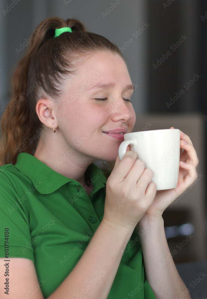 Happy young woman drinking a cup of tea. Dreaming girl sitting in living room with cup of hot coffee enjoying. Pretty woman home.Vertical photo Happy young woman drinking a cup of tea. Dreaming girl sitting in living room with cup of hot coffee enjoying. Pretty woman home.Vertical photo