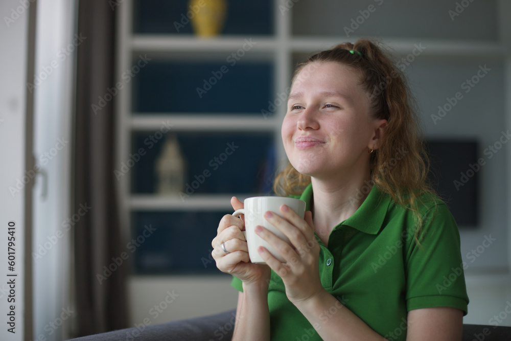 Happy young woman drinking a cup of tea. Dreaming girl sitting in living room with cup of hot coffee enjoying. Pretty woman home. Happy young woman drinking a cup of tea. Dreaming girl sitting in living room with cup of hot coffee enjoying. Pretty woman home.