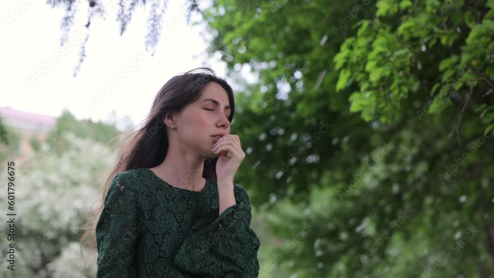 A beautiful and joyful brunette woman in a green dress stands in front of a green garden. the petals of blossoming fruit trees fall in the background. A beautiful and joyful brunette woman in a green dress stands in front of a green garden. the petals of blossoming fruit trees fall in the background.