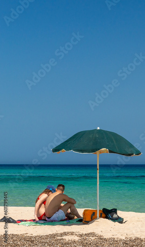 Couple of young persons on the beach with umbrella on golden sand with blue sky and crystal turquoise sea. © PAOLO