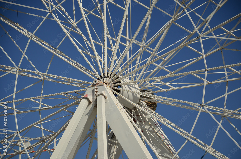 View of the steel structure of a fairground ferris wheel, with the axis, the spokes and the blue sky in the background View of the steel structure of a fairground ferris wheel, with the axis, the spokes and the blue sky in the background