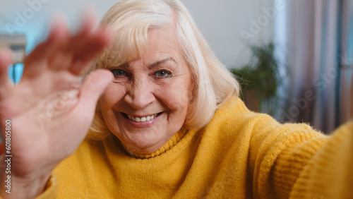 POV of senior grandmother woman making online selfie video call talking waving hand looking at camera at home apartment indoors. Communication, meeting. Elderly blogger making smartphone conversation
