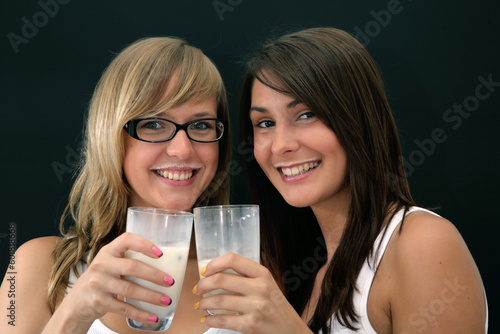 two girls over black background with glasses of milk and mustaches