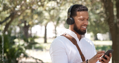 Businessman, typing and phone music in nature, communication and chat in the morning. Smile, young and employee listening to a podcast, radio or streaming audio on a mobile in a park for a commute