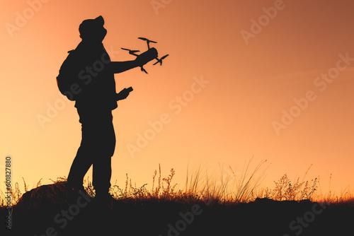 outside, the silhouette of a man with a quadcopter in his hands looks into the sky to launch a drone