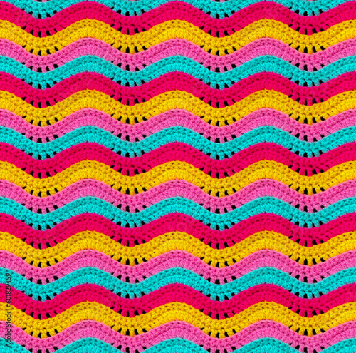 Seamless knitted pattern in the form of openwork waves is crocheted with threads of bright colors. Acrylic baby yarn. Volumetric style.