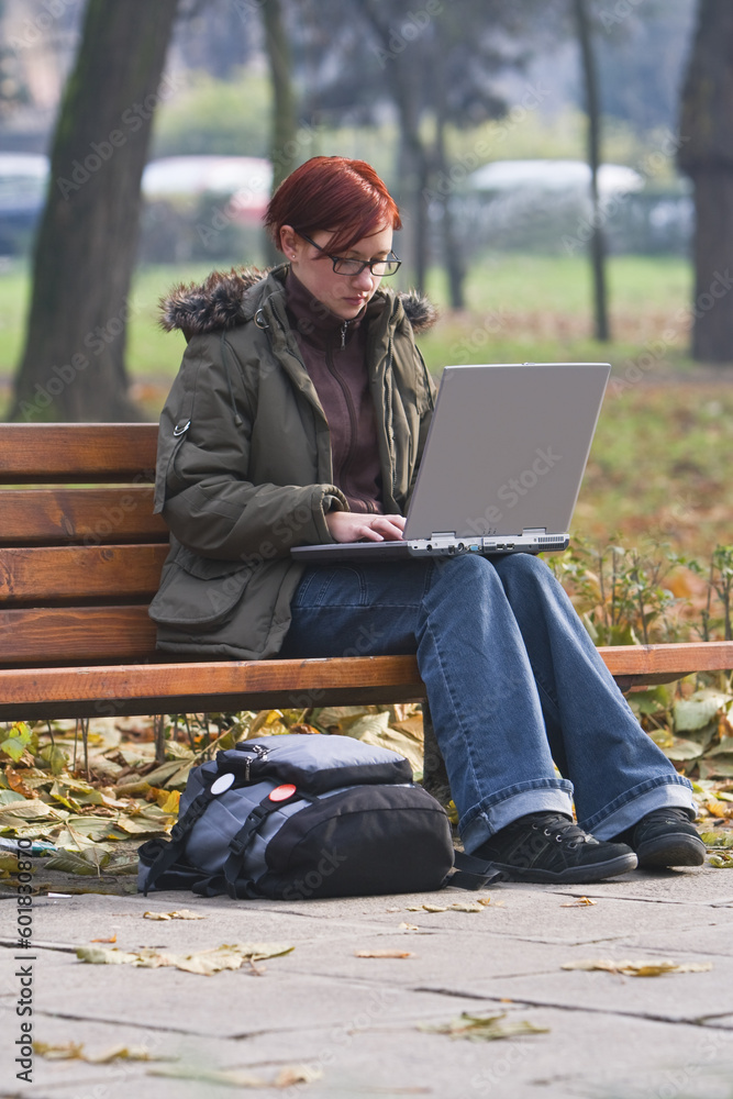 Redhead girl working on a laptop in an autumn park.
