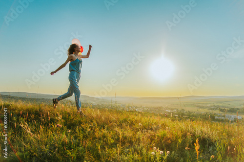 Woman running on a hill at sunset with balloons