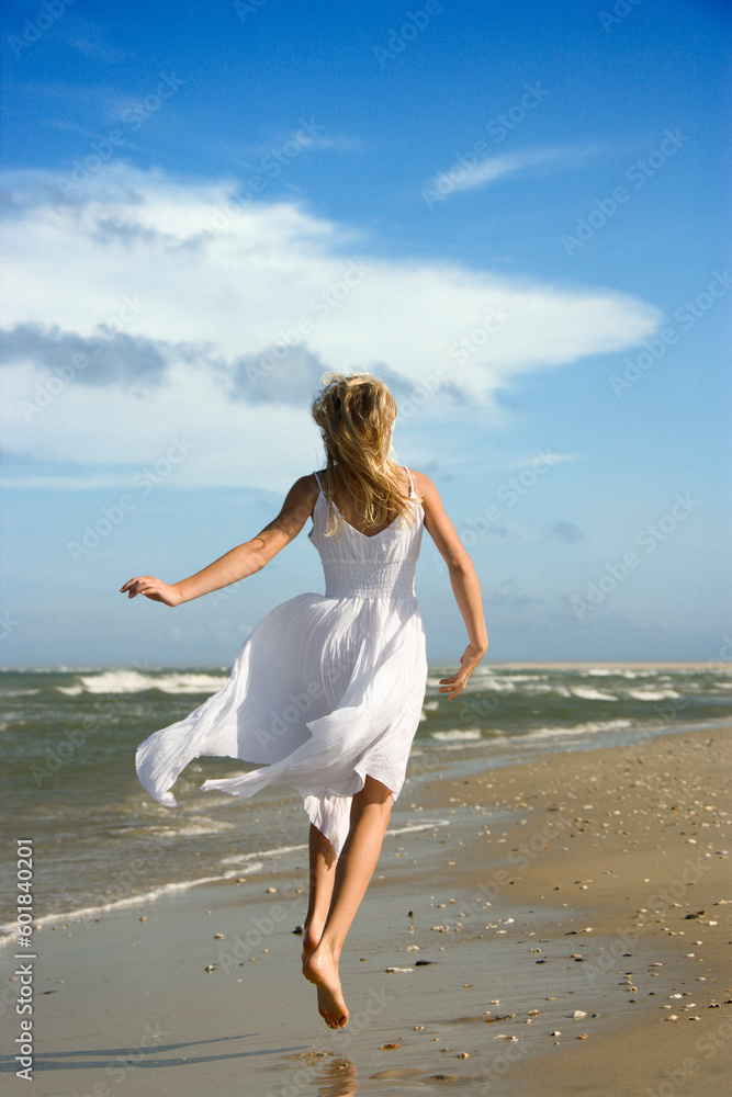 Caucasian pre-teen girl running down the beach in flowing white dress. Caucasian pre-teen girl running down the beach in flowing white dress.