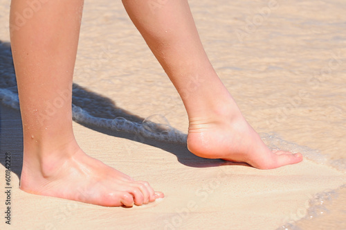 Feet of a young woman touching water on tropical beach