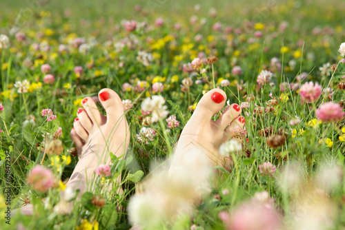 Fototapete Female feet with a pedicure on a summer blossoming lawn
