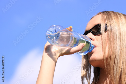 Girl drinking water against blue sky in sunny day