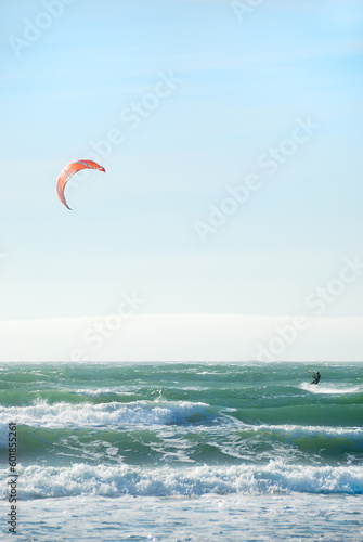 Surfer with red kite surfing off the beach in San Francisco, California on a sunny day.