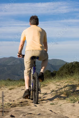 Obraz Man riding bicycle on the beach with hills in the background