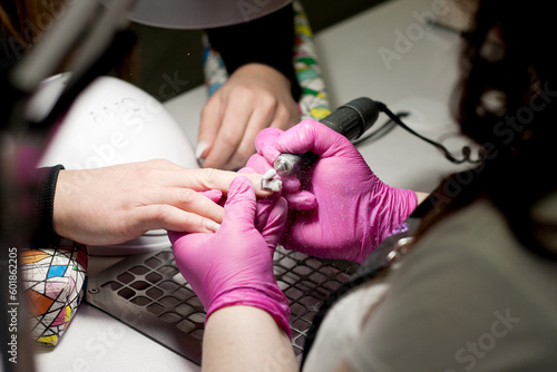 Salon manicure. Professional hardware manicure. Closeup of hands of manicurist in pink gloves uses electric drill to remove gel polish on hands during manicure. Dust when removing varnish.
