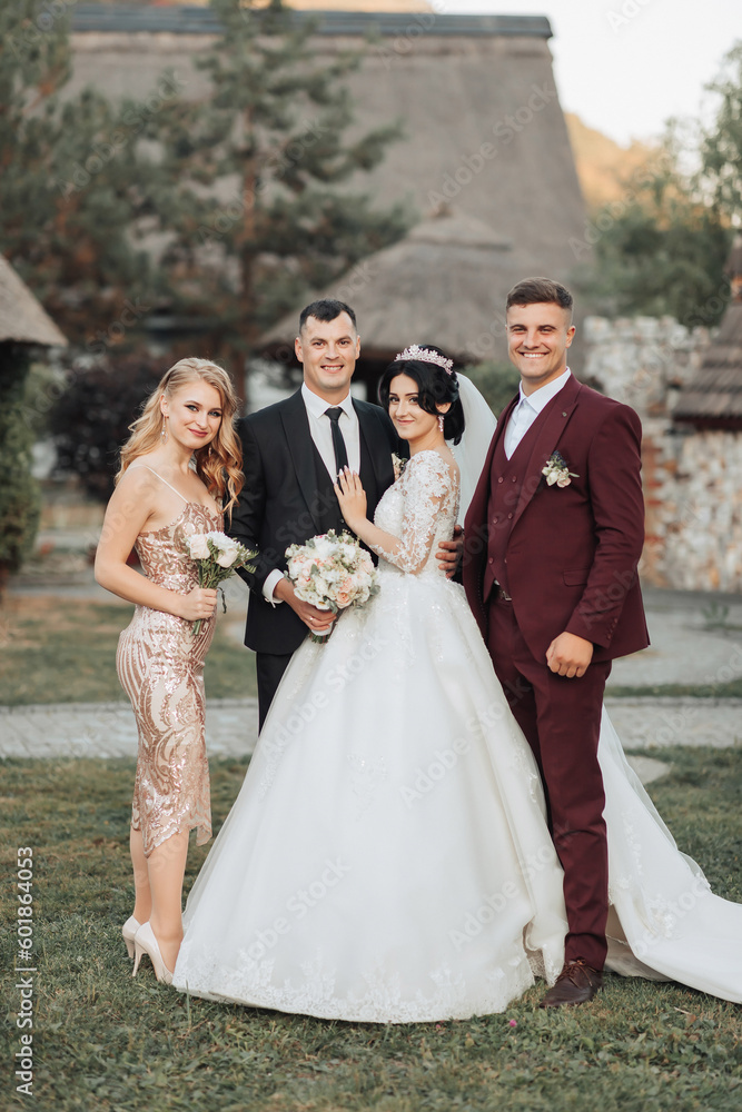 Wedding portrait. Front view of newlyweds walking hand in hand among friends. Girls in golden dresses hold bouquets, the bride in a voluminous dress, the groom and his friends in suits. Wedding portrait. Front view of newlyweds walking hand in hand among friends. Girls in golden dresses hold bouquets, the bride in a voluminous dress, the groom and his friends in suits.