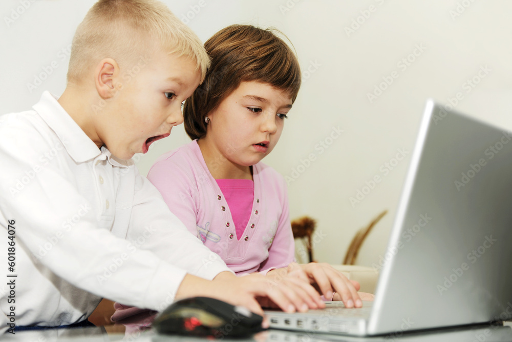 two happy children playing games and learnig education lessons on laptop computer at home