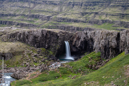 Scenic view of the waterfall flowing between green cliffs in Iceland