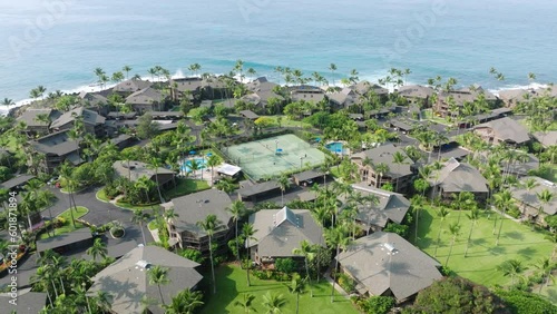 Drone flying above tennis court with active game match, Hawaii USA summer trip 4K. Background of tennis court in tropical lavish green garden of resort hotel area with beach villas or cottages photo