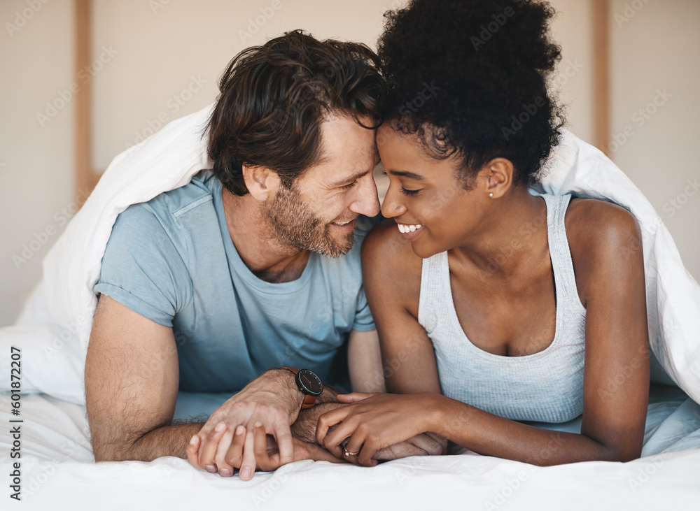 Happy interracial couple, bed and intimate morning in relax or bonding relationship at home. Man and woman smiling in joyful happiness for love, affection or relaxing weekend together in the bedroom - obrazy, fototapety, plakaty 