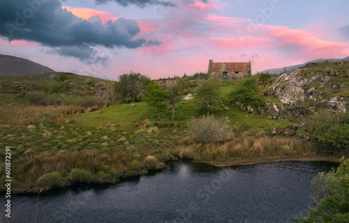 Fototapeta Naklejka Na Ścianę i Meble -  Breathtaking landscape sunrise scenery of old rusty tin roof cottage by the river with mountains in the background at Connemara National park in county Galway, Ireland 