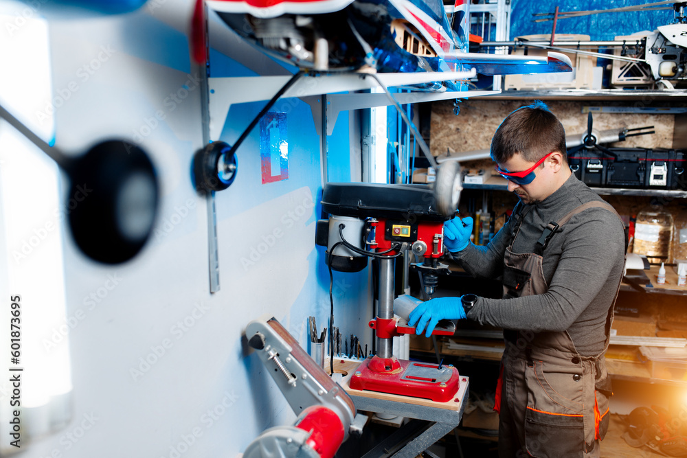 Fototapeta premium Male engineer or technician using drill for drone details in lab. Aircraft capable of GPS surveillance. Carbon.