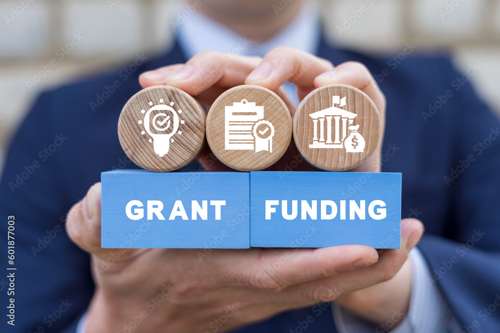Man holding colorful blocks with icons and inscription: GRANT FUNDING. Concept of grants and funding.