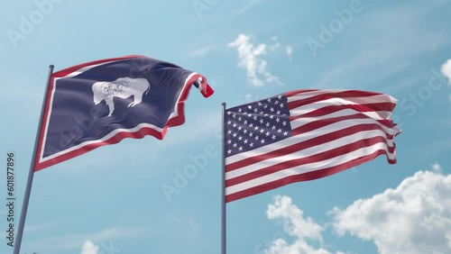 Wyoming flag and the USA flag on a flagpole realistic wave on strong wind in blue sky. State of Wyoming and The United States of America