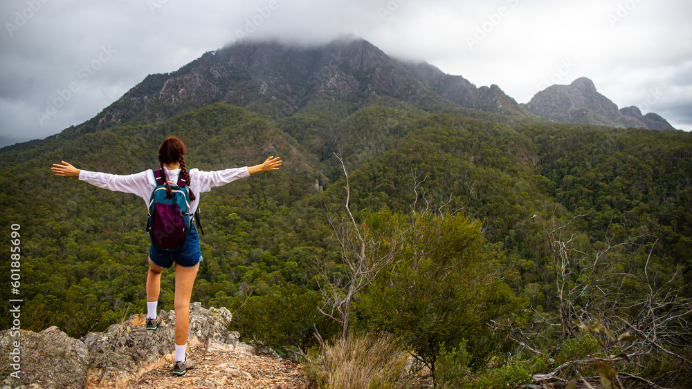A beautiful girl with her arms outstretched admires the famous Mount Barney from Yellow Pinch Lookout, Mount Barney National Park, Brisbane, Queensland
