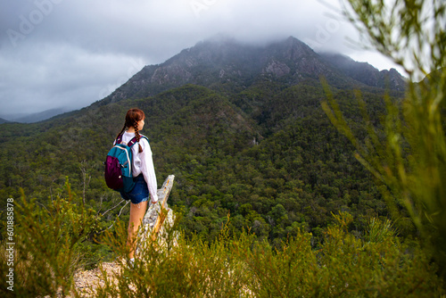 beautiful and brave girl standing at the top of the hill with large mountain in front of her; mighty mount barney in queensland, australia seen from yellow pinch lookout