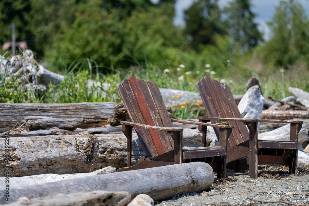 Empty adirondack chairs sit amongst driftwood on a rocky beach. Empty adirondack chairs sit amongst driftwood on a rocky beach.