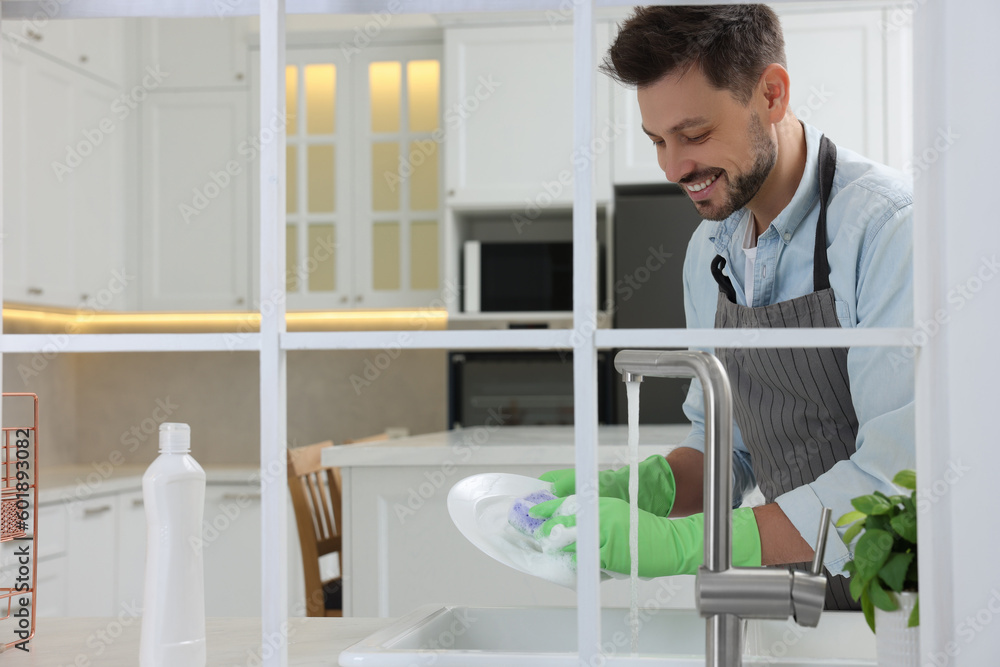 Man washing plate above sink in kitchen, view from outside Man washing plate above sink in kitchen, view from outside