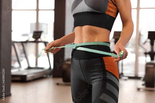 Slim woman measuring waist with tape in gym, closeup