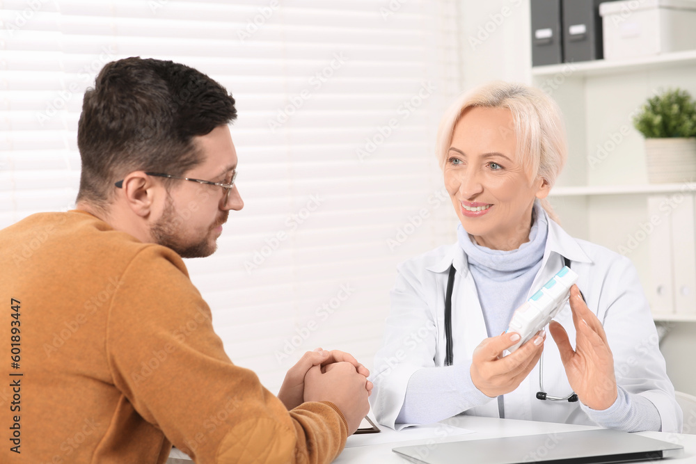 Doctor holding box of pills and consulting patient at white table in clinic Doctor holding box of pills and consulting patient at white table in clinic
