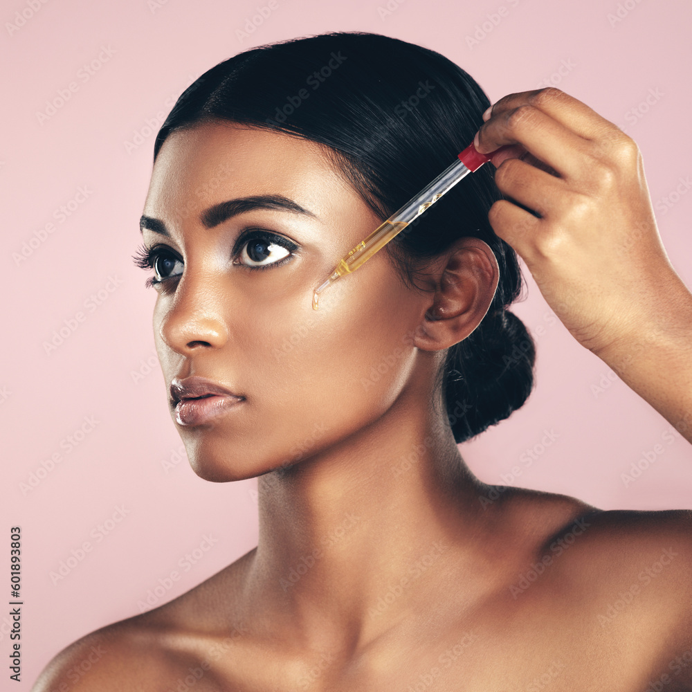 Obraz premium Face, skincare serum and woman in studio isolated on a pink background. Dermatology, cosmetics and Indian model with hyaluronic acid, essential oil or vitamin c dropper for healthy skin and beauty.