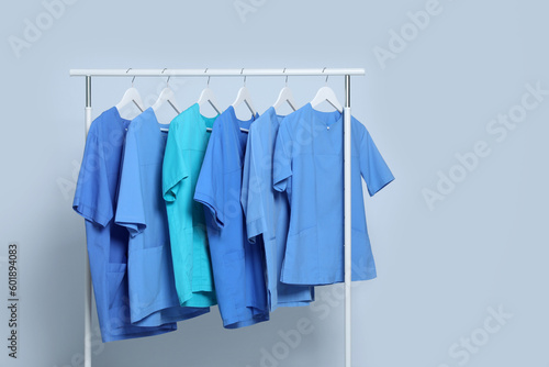Different medical uniforms on rack against light grey background. Space for text
